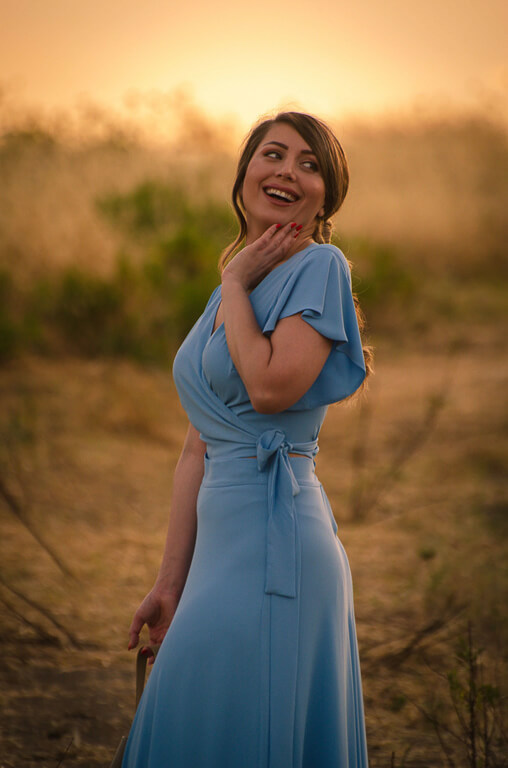 a woman holding her yellow dress to the side in a field with purple flowers and a blue sky