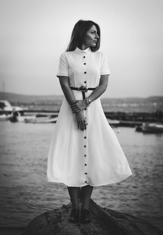 black and white photo of a woman on the side looking at the camera wearing a shirt and a skirt