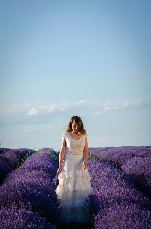 woman in a white dress outside with purple flowers and a blue sky