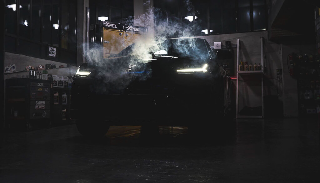 A black Lamborghini jeep in a garage with smoke and the lights on from a diagonal position