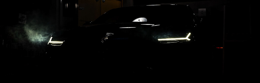 a dark black Lamborghini jeep in a garage with the lights on from a diagonal position and the sign