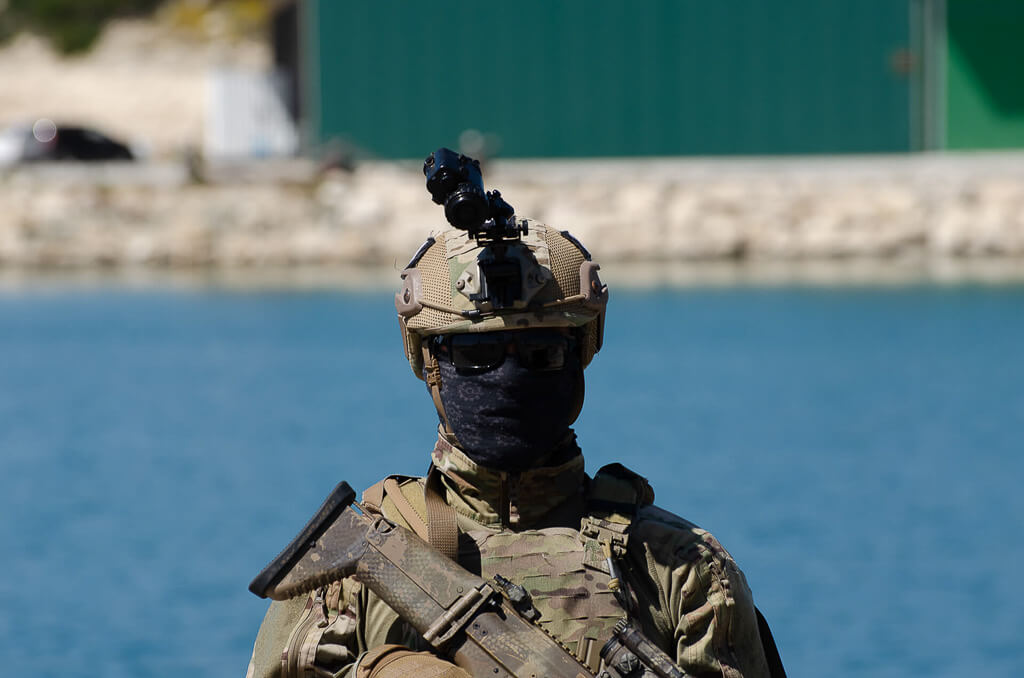 a soldier in uniform, mask, black glasses, helmet, and camera on his helmet holding a weapon