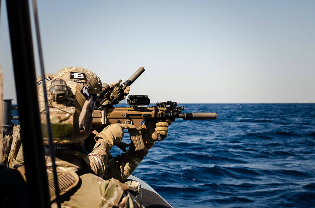 soldiers in a war boat with uniforms and helmets holding automatic weapons and aiming.