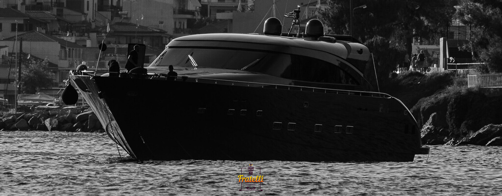 white and black photo with a black boat in the sea and houses in the background