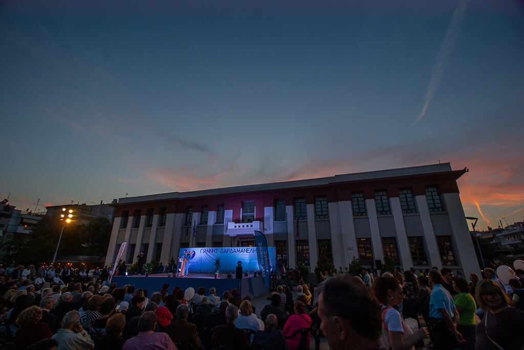 speech of Mayor Dardamanelis on the stage at the town hall. Below people watching the speech