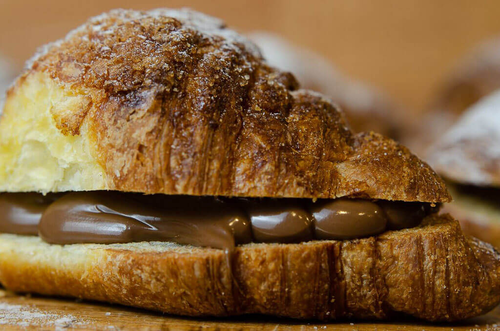 croissant on the side with chocolate filling and the icing on top, on a wooden base.