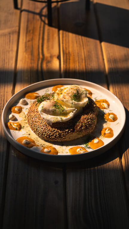 white plate with a salted pretzel and two fried eggs on a wooden table in the sunlight