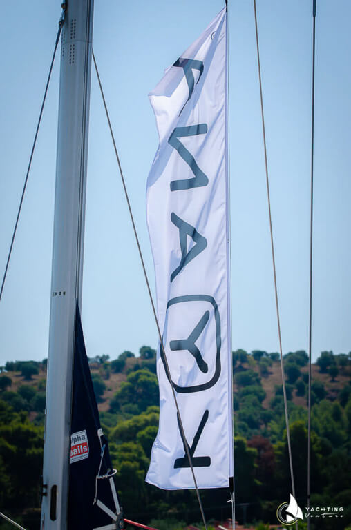 white flag Yachting Venture on a sailing boat and behind a mountain with trees.