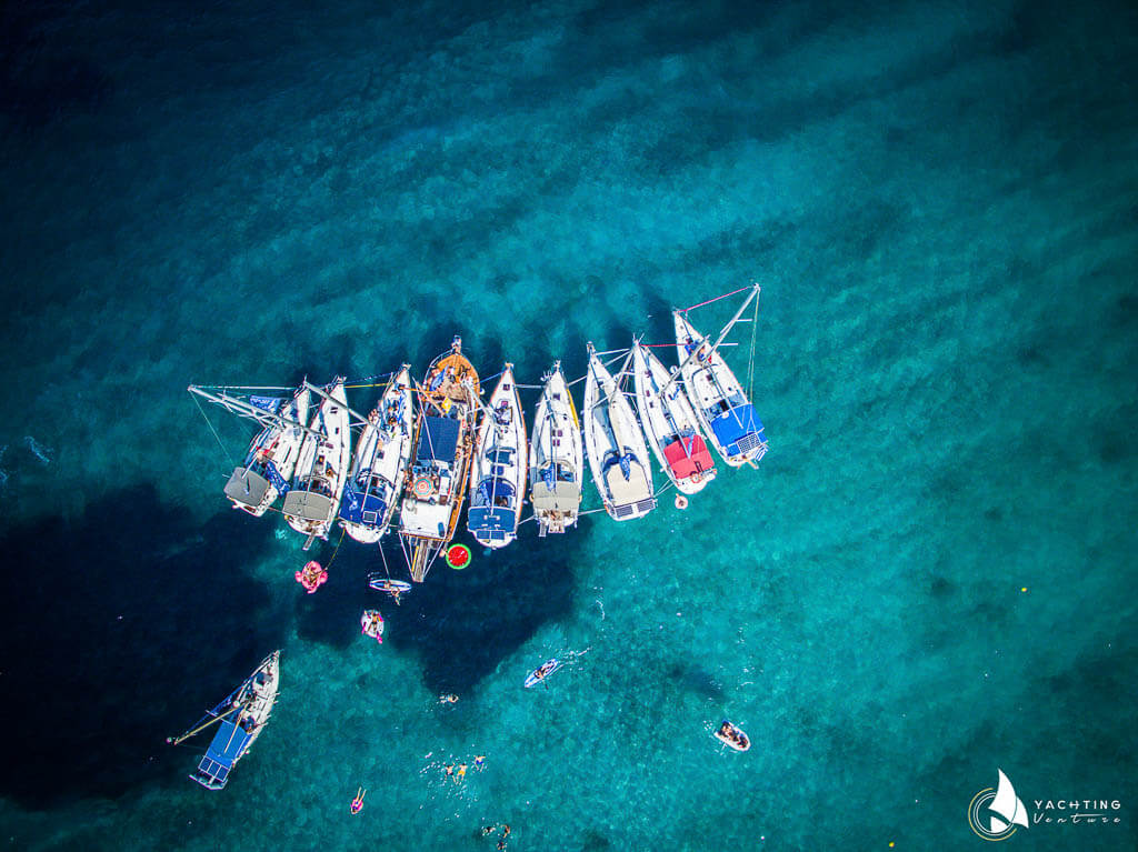 panoramic drone photo showing 10 boats in the blue sea and people swimming around.