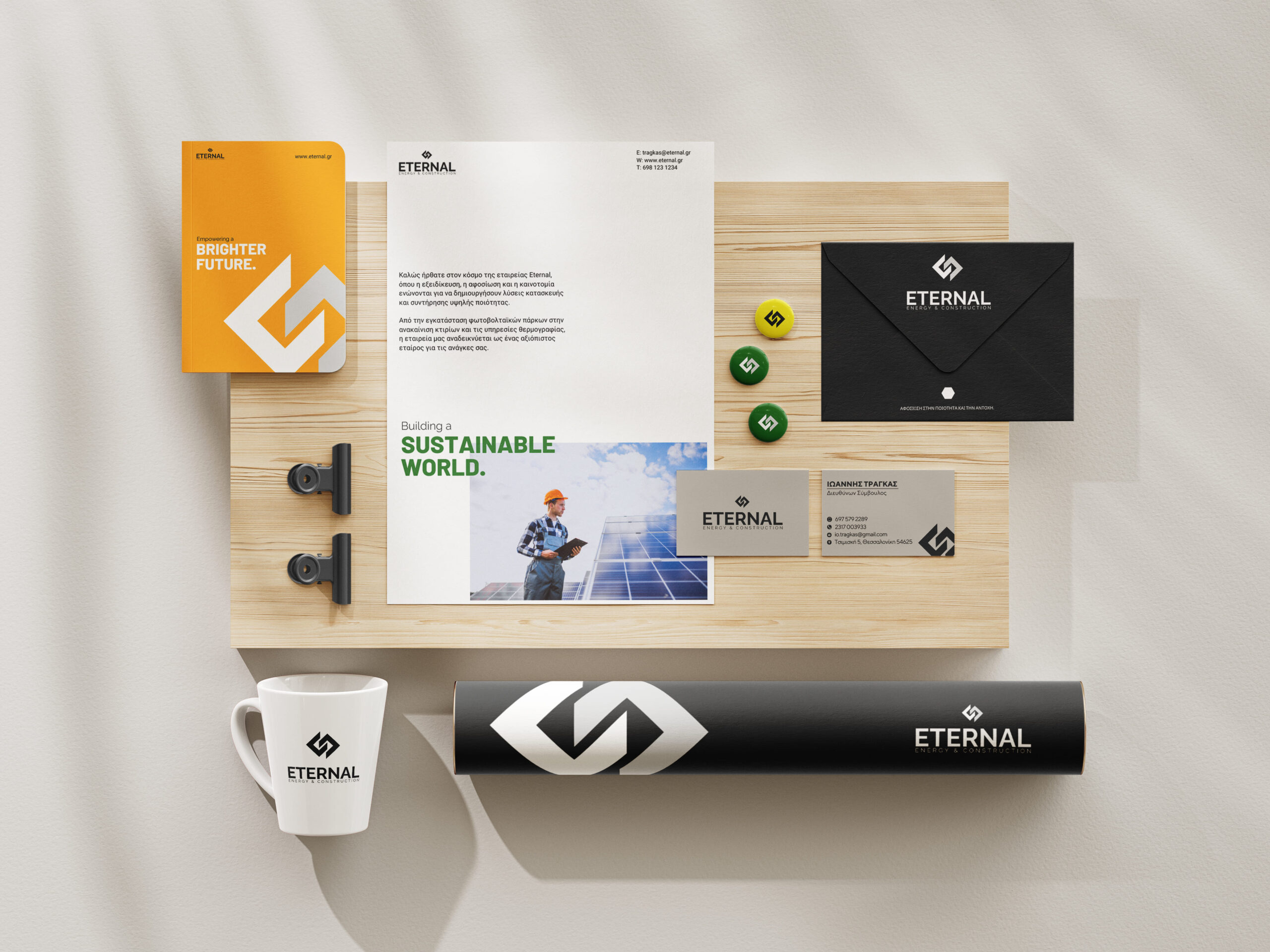 presentation of eternal corporate cards in grey black color, glass with the eternal logo, book in orange color with the logo, black envelope and 3 green and yellow badges with the logo.