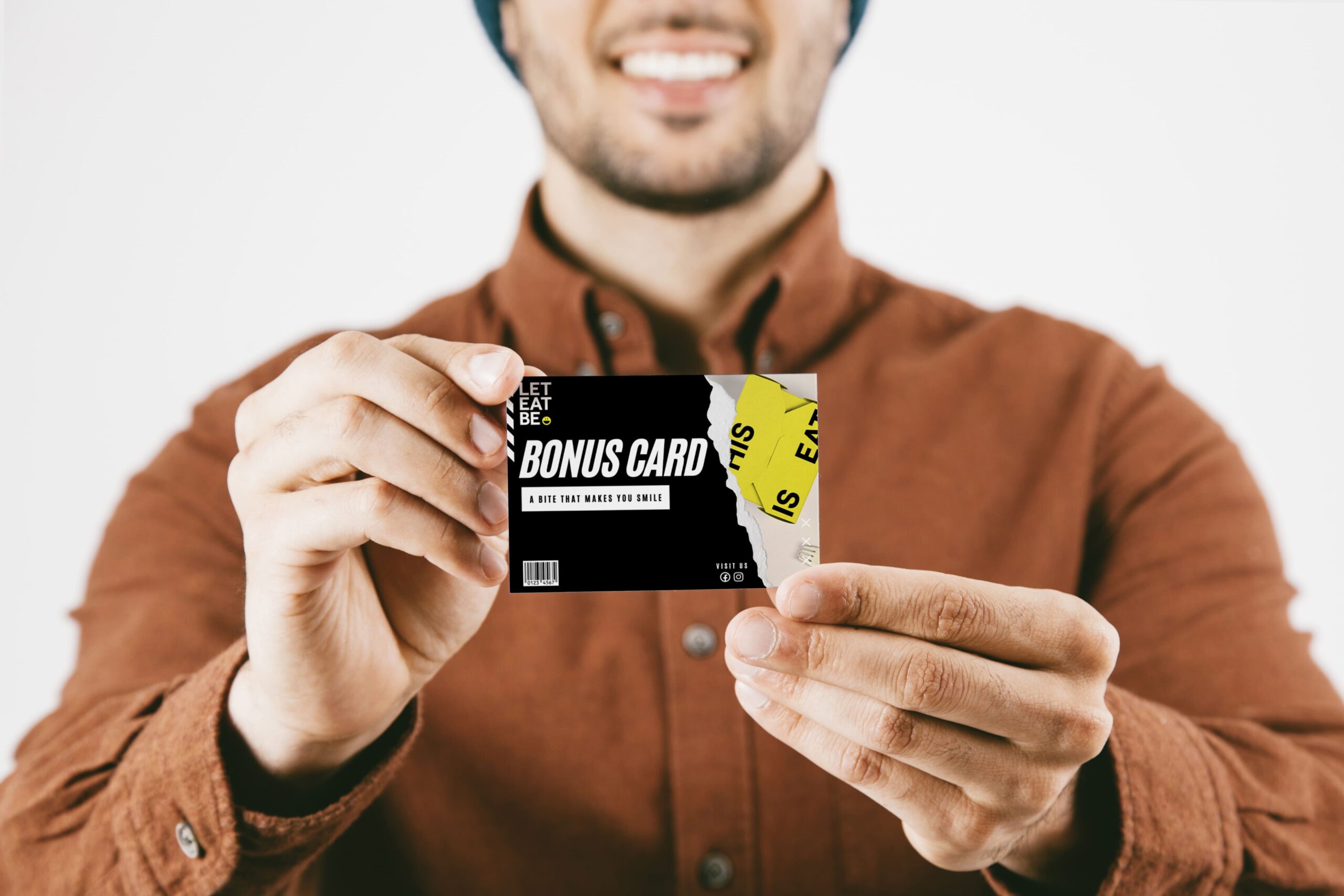 One man holding Bonus Cards Let Eat Be and smiling. Wearing an orange shirt and a cap.