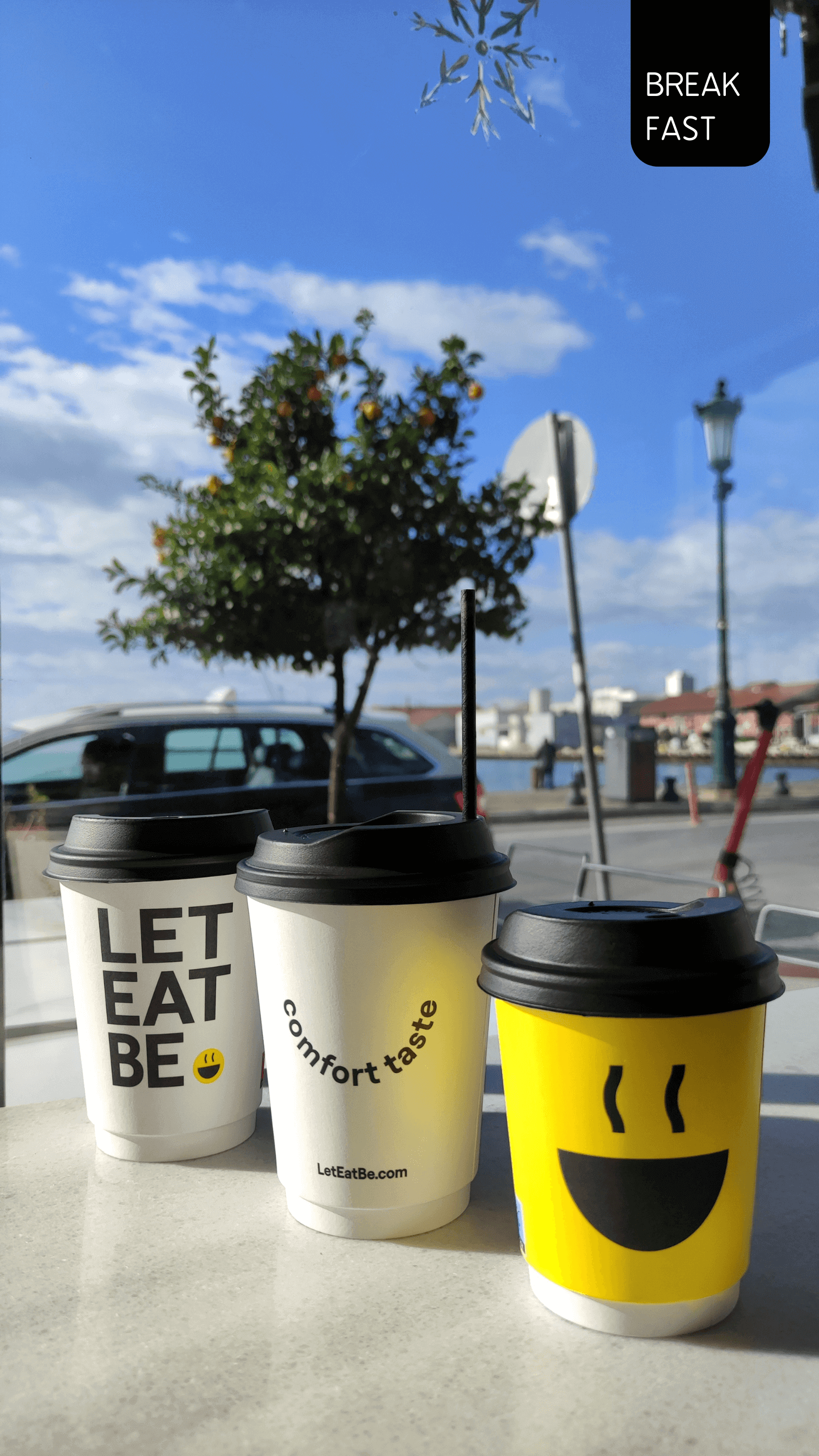 A table with three cups of coffee with yellow, black and white colors. Behing is the sea and the blue sky.